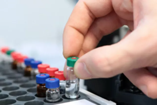 A hand picking up a test tube from a container in a lab. Photo.